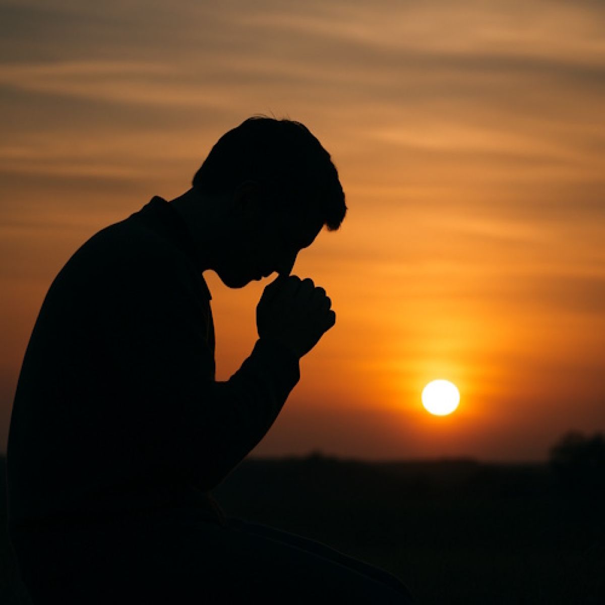 Silhouette of a person praying at sunset.