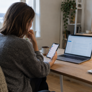 Arbeidstaker vurderer privat e-post på mobilen ved siden av bedriftens e-post på en bærbar PC